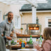 father and daughter laughing in the backyard with image focus on the pizza oven